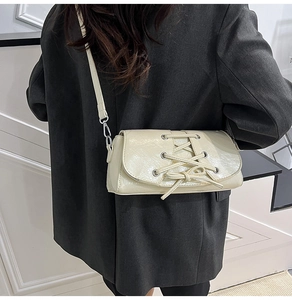 Detail of cream white shoulder bag with decorative lacing on grey blazer