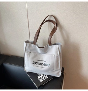 Detail of grey canvas tote bag with brown leather handles and exterior pocket on a sofa