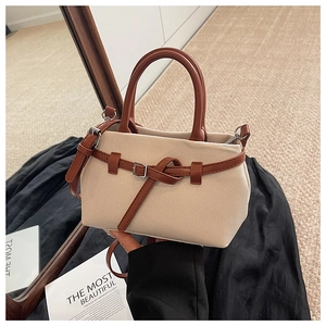 Detail of a chic bucket bag with cream woven texture, brown leather straps, and metal buckle