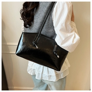 Close-up of black glossy tote bag featuring knot decor with silver metal ends on model