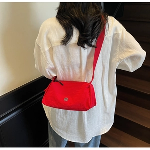 Detail of red nylon crossbody bag featuring a round metallic logo and wide woven strap