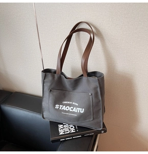 Detail of dark grey canvas tote bag featuring brown leather handles and a large snap pocket