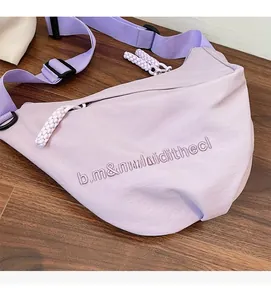 Detail of light purple nylon crossbody bag featuring letter embroidery and woven zipper pull