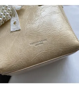 Détail d'un sac à main beige en cuir plissé avec texte embossé et ruban en perles et dentelle