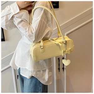 Detail of soft yellow leather baguette bag with a bow decoration and heart pendant