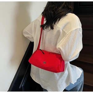 Detail of red nylon crossbody bag showing round metal logo and woven shoulder strap