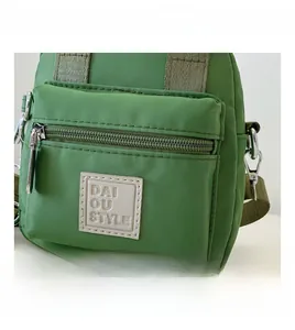 Detail view of water-resistant green nylon crossbody bag with zipper and logo patch