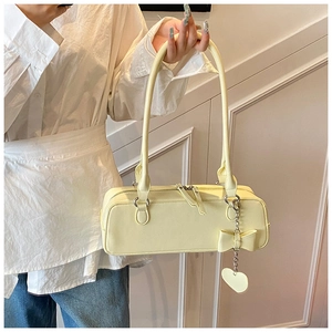 Detail of light yellow baguette bag with smooth faux leather and heart charm pendant