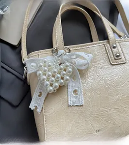 Détail d'un pendentif cœur en perles blanches avec nœud en dentelle sur sac beige