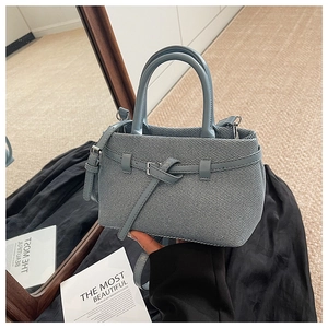 Close-up of a light blue denim bucket bag with leather buckle and adjustable strap