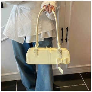 Detail of light yellow baguette bag with heart pendant and bow on side of matte leather