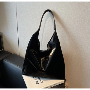 Detailed close-up of a glossy black minimalist hobo tote bag on a stylish leather sofa