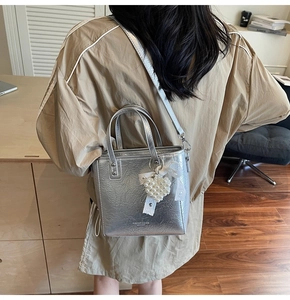 Détail du sac cabas argenté avec texture naturelle et breloque cœur perle sur modèle