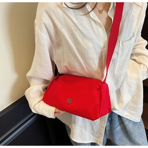 Close-up of red nylon crossbody bag with circular metal M logo and wide fabric strap