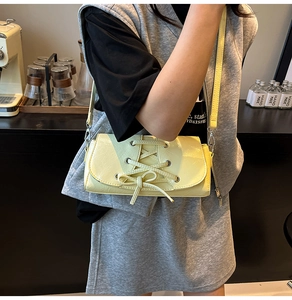 Detail of light yellow patent leather shoulder bag with chic lace-up bow and glossy finish