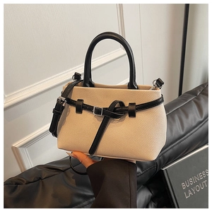 Detail of beige woven bucket bag with black leather straps and metal buckle accent