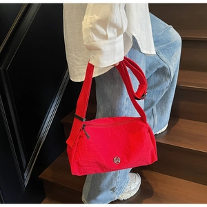 Red nylon crossbody bag with M logo shown on a model climbing stairs in a stylish setting