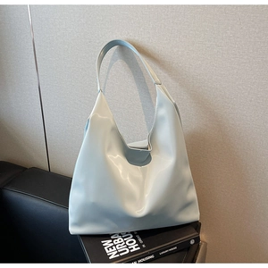 Detail of the light blue minimalist leather hobo bag placed on a book and dark sofa