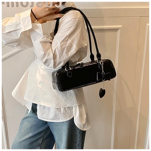 Detail of black patent leather baguette bag with bow and heart pendant on shoulder