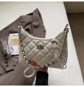 Detail der weißen Stepptasche mit silbernem Drehverschluss und dekorativer Metallkette