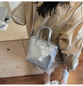 Détail du sac seau métallisé argenté avec nœud en dentelle et breloque cœur perle
