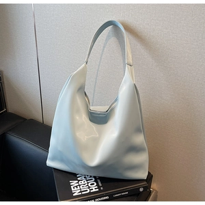 Detailed close-up of light blue hobo tote bag placed on a black leather sofa