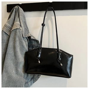 Glossy black underarm bag with unique knotted strap detail shown in a lifestyle setting