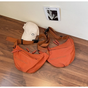 Detail of orange canvas dumpling bag featuring embroidered letters and woven shoulder strap