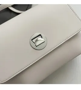 Detail view of cream white shoulder bag featuring a silver round twist lock and neat stitching