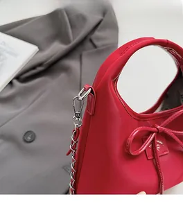 Détail d'un sac à main rouge brillant avec nœud et chaîne argentée sur un blazer gris
