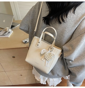 Détail du sac seau en cuir crème avec breloque cœur en perles et bandoulière