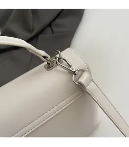 Close-up of silver metal hardware and fine stitching on ivory crossbody messenger bag