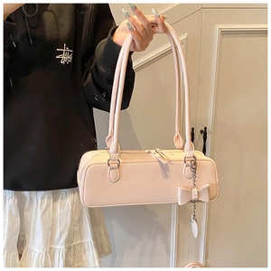 Close-up of light pink leather shoulder bag with a delicate bow charm and zipper