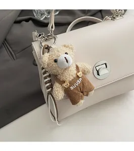 Detail of a plush bear charm in beige sherpa and corduroy hanging on a leather handbag