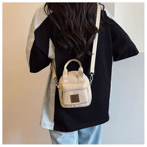 Detail view of mini nylon crossbody bag in off-white shown on a model's back