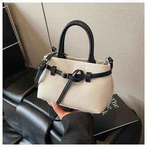 Detail of canvas bucket bag with black leather trim and metallic buckle on grey background