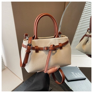Detail of beige canvas bucket bag with brown leather trim and metallic buckle closure
