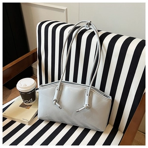 Detail of grey-blue shoulder bag with knotted strap and metal tip on a striped chair