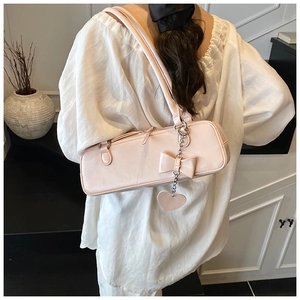 Macro view of peach pink shoulder bag featuring a decorative bow and silver heart chain charm