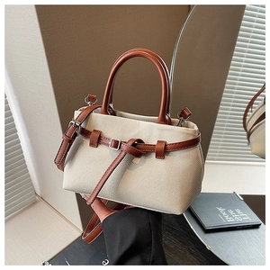 Detailed shot of beige canvas bucket bag with brown leather handles and buckle strap