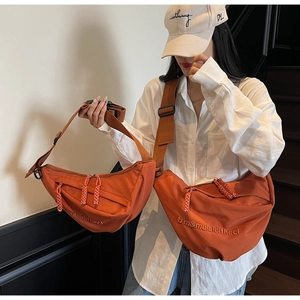 Detail of orange canvas crescent bag with letter embroidery and woven zipper pull