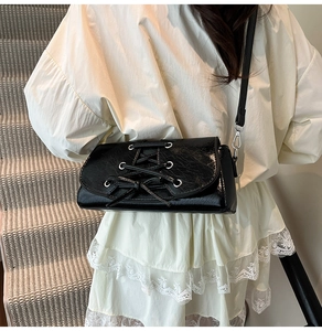 Detail of black patent leather shoulder bag with corset lace-up design and silver eyelets