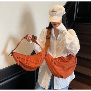 Close-up of orange canvas crescent crossbody bags in two sizes worn by a female model