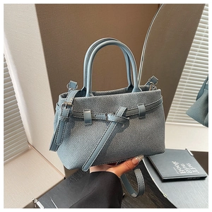 Detail of light blue textured fabric bucket bag with leather strap and top handles