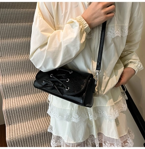 Detail of black crossbody bag featuring lace-up design with silver metal eyelets