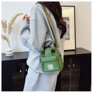 Close-up of green nylon crossbody bag featuring front zipper pocket and logo label