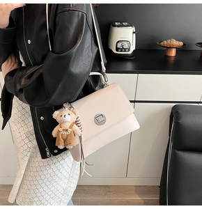 Close-up of cream square bag with silver rotary lock and cute bear plush charm