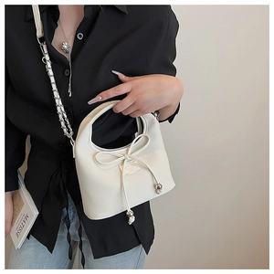 Détail du sac demi-lune blanc avec nœud, chaîne et plaque logo porté par le modèle