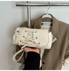 Close-up of cream shoulder bag with corset lacing detail and silver metal eyelets