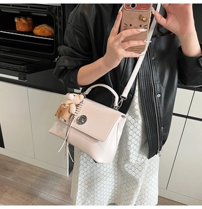 Detail of a beige leather crossbody bag featuring a silver twist lock and plush bear charm